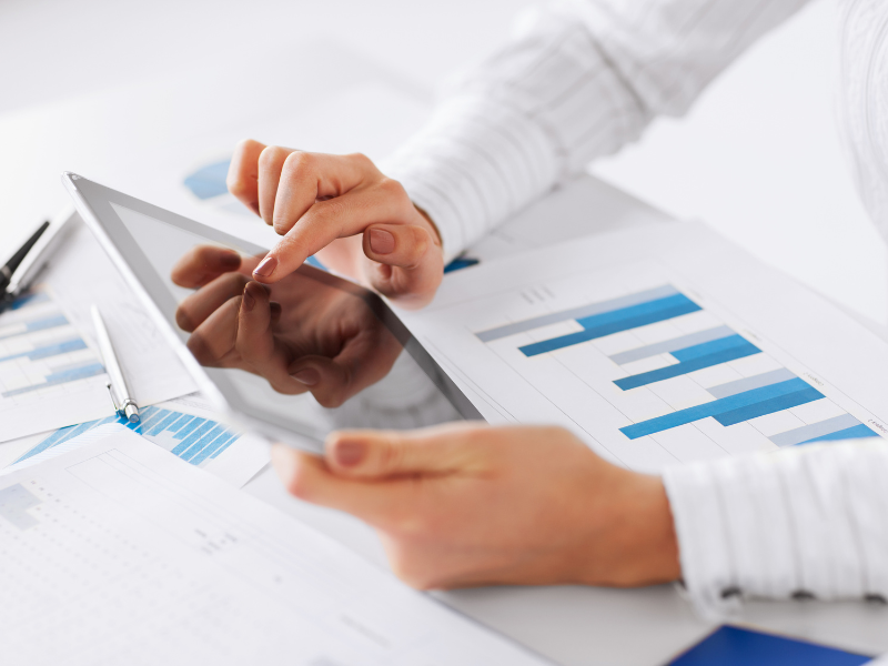 Close-up of hands using a tablet with forecasting charts and graphs on paper.